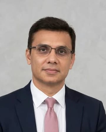 Portrait of Mr. Kartik Broker, wearing glasses, a navy suit and a pink tie