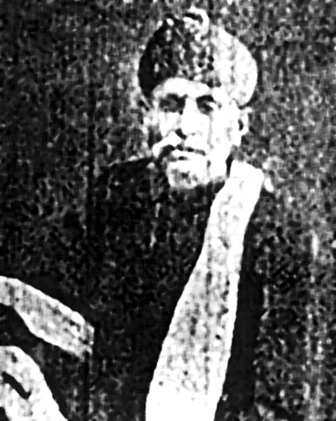 Archive photograph of the late Mr. Nemidas Hemchand, seated, wearing a turban and a long shawl