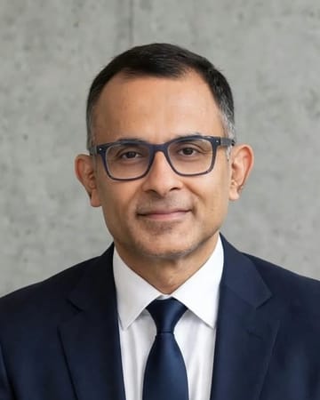 Portrait of Mr. Udayan Broker, wearing dark-rimmed glasses, a navy suit and a navy tie